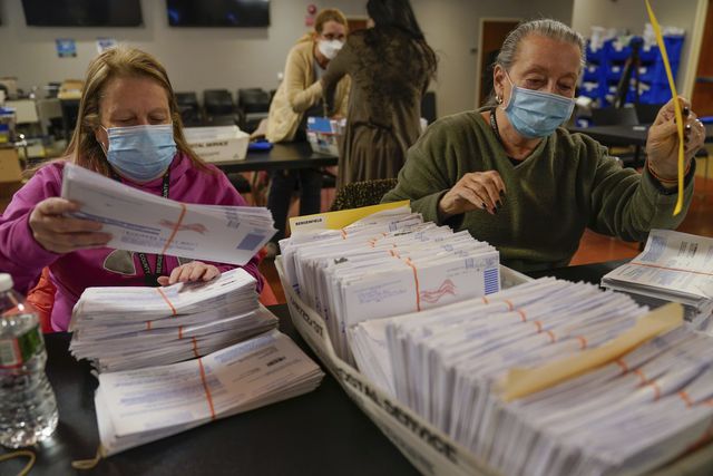 Election workers go through stacks of mail-in ballots